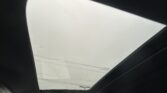 View from inside a car through a panoramic sunroof, showing a cloudy sky and papers resting on the glass surface.”,