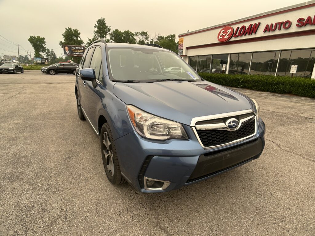 Blue SUV parked diagonally in a dealership lot with the EZ Loan Auto building sign visible in the background behind the car window. Random cars line the lot and trees are further back.