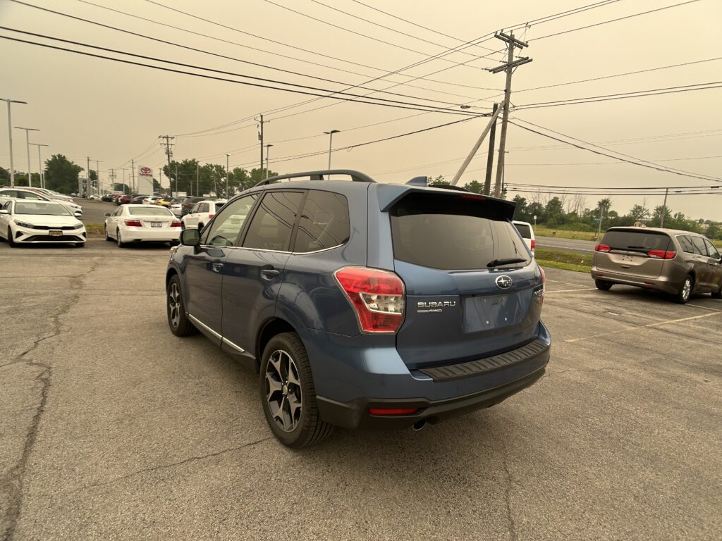 Blue Subaru SUV in a car dealership lot with other vehicles and utility poles in the background.