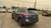 Blue Subaru SUV in a car dealership lot with other vehicles and utility poles in the background.