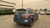 Blue Subaru Forester XT parked in a car lot beside a white building with large glass windows and overhead power lines.