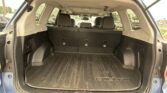 Rear cargo area of a Subaru SUV with third-row seats upright, black rubber cargo mat, and visible parking lot outside the vehicle.