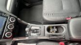 Interior of a car showing the driver’s seat, center console with gear shifter, climate control dials, and cup holders; a paper mat lies on the floor.