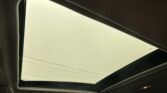 Interior of a car ceiling with a large panoramic sunroof, showing light sky through the glass paneled roof.