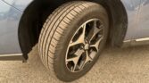 Close-up of a car tire and alloy wheel in the wheel well, with gravel road underneath.