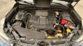 Open car hood shows the engine bay with the battery on the right and yellow‑caps for fluid reservoirs visible.