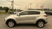 Silver Kia SUV in a dealership parking lot with overhead power lines and a dealership sign in the background.