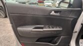 Door panel of a car interior with window controls and speaker; outside the window, a parking lot with several parked cars is visible.