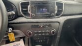 Center console of a car with a touchscreen displaying 2:31 PM, surrounded by radio controls and climate dials; papers on the passenger footwell visible below.
