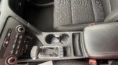 Front interior of a car showing the center console with gear lever, cup holders, and climate control dials over dark fabric seats.