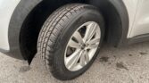 Close-up of a car tire and alloy wheel on a light-colored vehicle, with water droplets on the fender and wheel well.