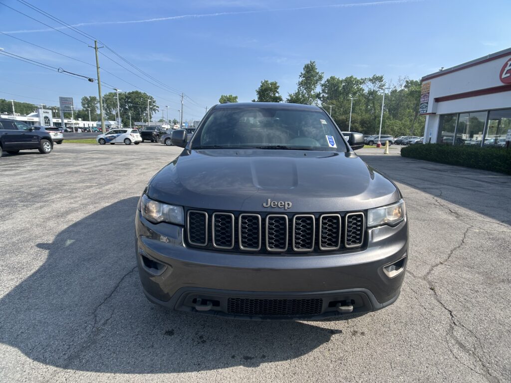 Front view of a gray Jeep SUV in a sunny dealership parking lot with other cars nearby.