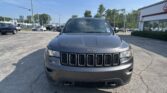 Front view of a gray Jeep SUV in a sunny dealership parking lot with other cars nearby.