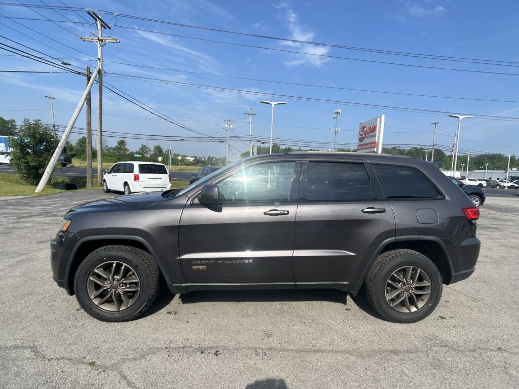 Gray Jeep Grand Cherokee parked in a dealership lot with power lines and a clear blue sky