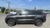 Gray Jeep Grand Cherokee parked in a dealership lot with power lines and a clear blue sky