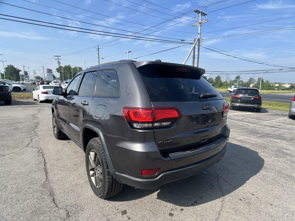 Rear view of a gray Jeep SUV in a parking lot with other cars and power lines overhead at a dealership.