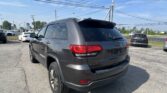 Rear view of a gray Jeep SUV in a parking lot with other cars and power lines overhead at a dealership.