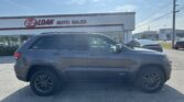 Gray Jeep Grand Cherokee SUV parked in front of an E-Z Loan Auto Sales storefront on a sunny day with a blue sky and power lines above.