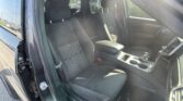 Interior of a black car showing front seats with red contrast stitching and center console, open driver-side door; sunny glare outside.
