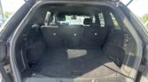 Open hatch reveals the cargo area of a dark SUV with the rear seats upright in an empty trunk, parking lot visible outside