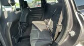 Interior of a car's back seat with three seats, headrests, and seat belts visible; outside you can see a parking lot through the windows.