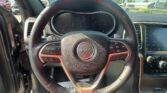 Driver's view of Jeep steering wheel with instrument cluster and infotainment screen; parking lot outside the windshield fall visible.