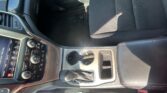 Interior of a car showing center console with gear shifter, cup holders, and infotainment screen beside a black fabric passenger seat.