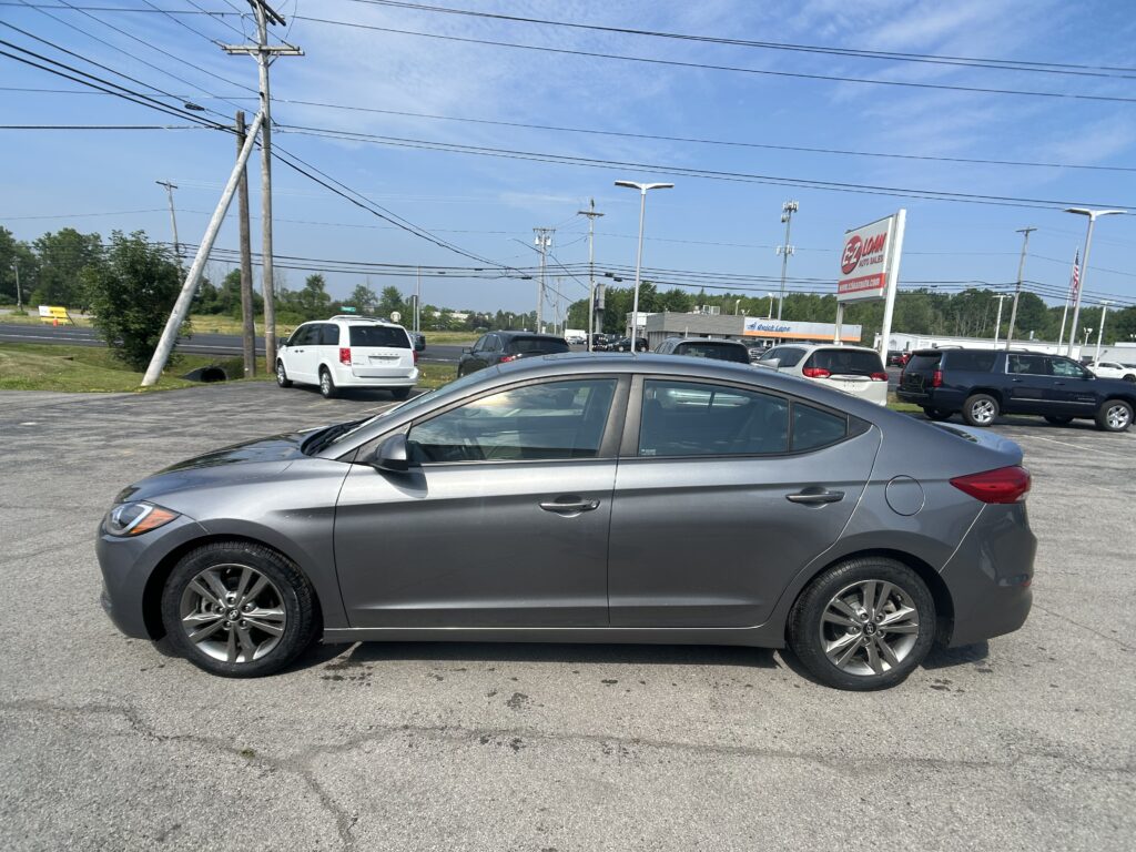 Silver sedan in a car dealership lot with several other vehicles, power lines overhead, and an EZ Loan Auto Sales sign in the background.