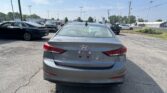 Rear view of a gray Hyundai Elantra in a busy car dealership lot with other cars in the background.