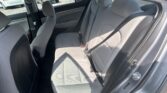 Rear passenger row of a gray car with three headrests, seat belts fastened, and light gray upholstery visible from the open door.