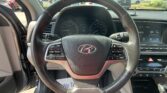 Driver's-eye view of a car interior: steering wheel centered, speedometer cluster and right touchscreen visible through the windshield.