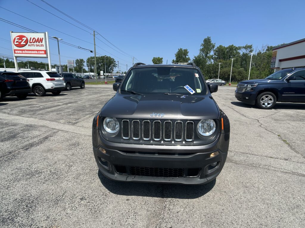 Front view of a gray Jeep in a car dealership parking lot with a red E-Z Loan sign in the background.