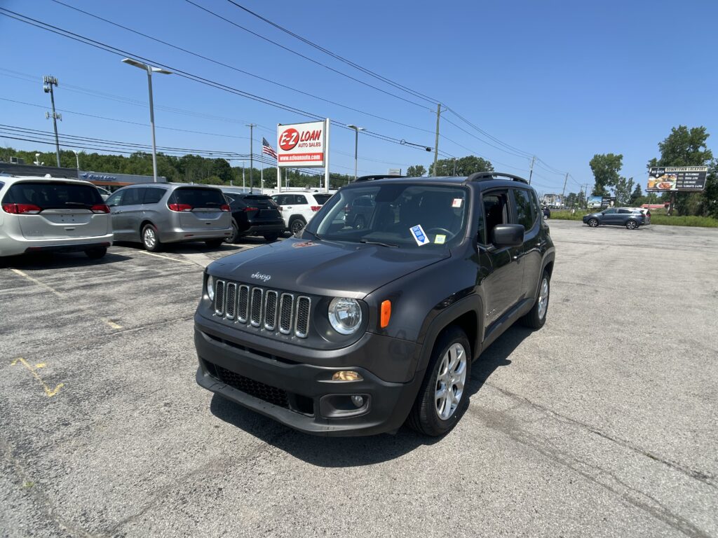 Front corner of a dark gray Jeep in a car lot with an EZ LOAN Auto Sales sign nearby on a sunny day.