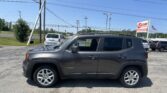 Gray Jeep Renegade parked in a dealership lot with power lines overhead and a blue sky above.