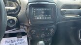 Interior of a car dashboard: touchscreen showing FM radio 106.5, climate controls below, start/stop button on the left, and a printed sheet on the passenger side.