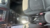 Interior of a car showing the center console with touchscreen on the left, gear shifter, cup holder, and front passenger seat with a red seatbelt buckle nearby