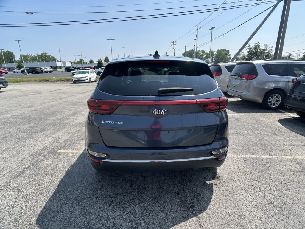 Rear view of a gray Kia Sportage parked in a crowded lot, with other cars and power lines in the background.