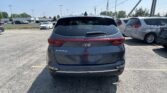 Rear view of a gray Kia Sportage parked in a crowded lot, with other cars and power lines in the background.