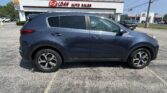 Blue Kia Sportage in the foreground at a car dealership lot in front of the E-Z Loan Auto Sales building.