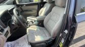 Interior of a dark SUV with gray cloth seats, steering wheel, and open driver’s door; outside a parking lot with other cars visible.