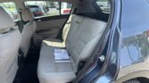 Open rear passenger door of a blue SUV, light gray fabric back seat with papers on the seat, visible outside cars in a lot.
