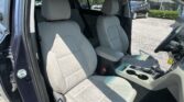 Interior of a right-hand-drive SUV showing light gray fabric front seats and center console, with a parking lot visible through the windows outside the open driver door.
