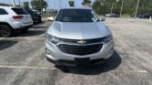 Front view of a silver Chevrolet SUV in a parking lot with other vehicles and a clear blue sky in the background.