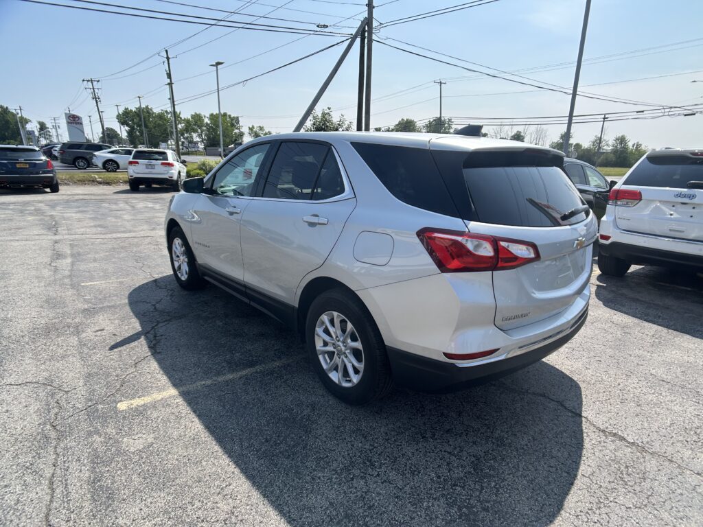 White Chevrolet Equinox SUV in a dealership parking lot with other cars and overhead power lines visible under a blue sky.