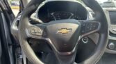 Interior view of a Chevy steering wheel and dashboard with the ignition button visible, driver-side door open, and outside parked cars.