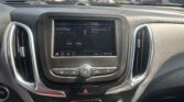View from center console of a car: infotainment screen showing radio and icons, with outside parking lot seen through windshield, dashboard and vents visible.