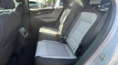 Rear passenger seat area of a car with gray quilted upholstery and headrests, seat belts fastened, view of parked cars outside through the window.