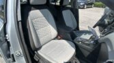 Front interior of a car showing light gray quilted seats, center console, and an open door with a parking lot visible outside.