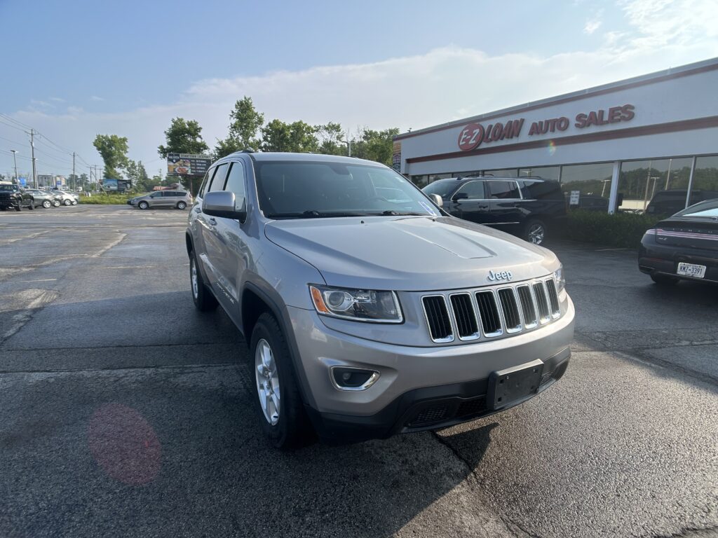Silver Jeep SUV in the foreground outside EZ Loan Auto Sales, with a row of parked cars and a blue sky above.