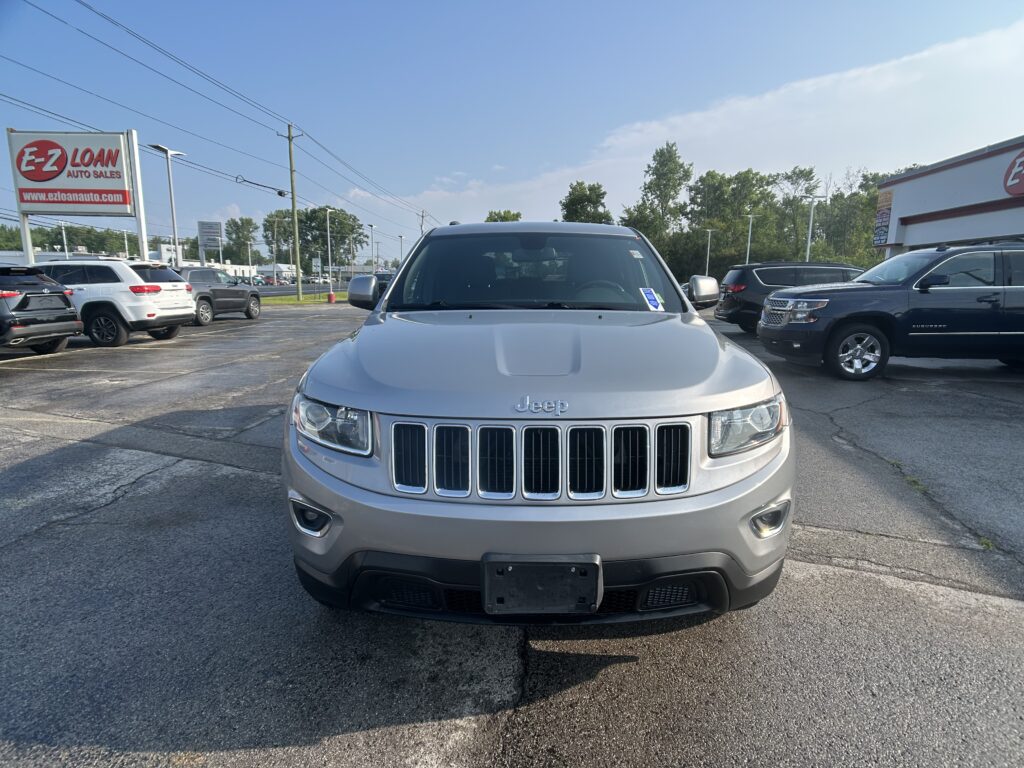 Front view of a silver Jeep SUV in a dealership lot, with an EZ LOAN Auto Sales sign on the left and other cars in the background.